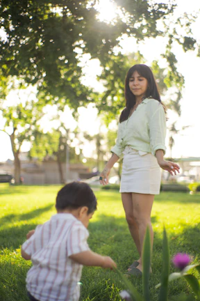 A smiling caregiver gently holding a child's hand in a sunny park.