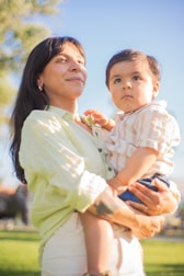Smiling mother holding her healthy child outdoors on a sunny day.