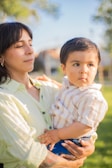 A smiling single mother holding her child gently in a sunlit garden.