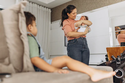 Mother holding baby while stretching in a softly lit room with white and lilac decor.