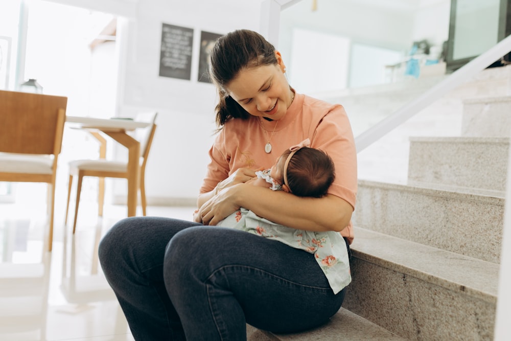 a woman holding a baby sitting on a set of stairs