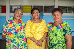A cheerful family concierge team dressed in 70s style outfits welcoming guests near the sea.