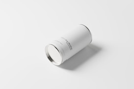 A plain white cylindrical can with minimal text lies on a light surface, casting a soft shadow to the side. The can appears to be a mockup design with simple and clean typography.