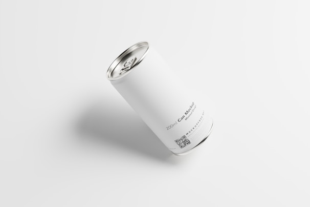 A white cylindrical can with a metallic top and bottom is placed on a light background. The can features minimal text and a QR code near the bottom. The text reads '200ml Can Mockup' along with a website URL.