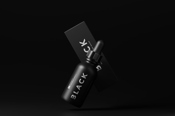 A black dropper bottle labeled 'BLACK' is positioned in front of a matching black box on a dark background, giving a sleek and minimalist appearance.