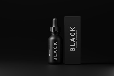 A minimalistic design featuring a black dropper bottle and a matching rectangular box both labeled with the word 'BLACK'. The overall aesthetic is sleek and modern, with smooth matte textures and white text contrasting against the dark background.