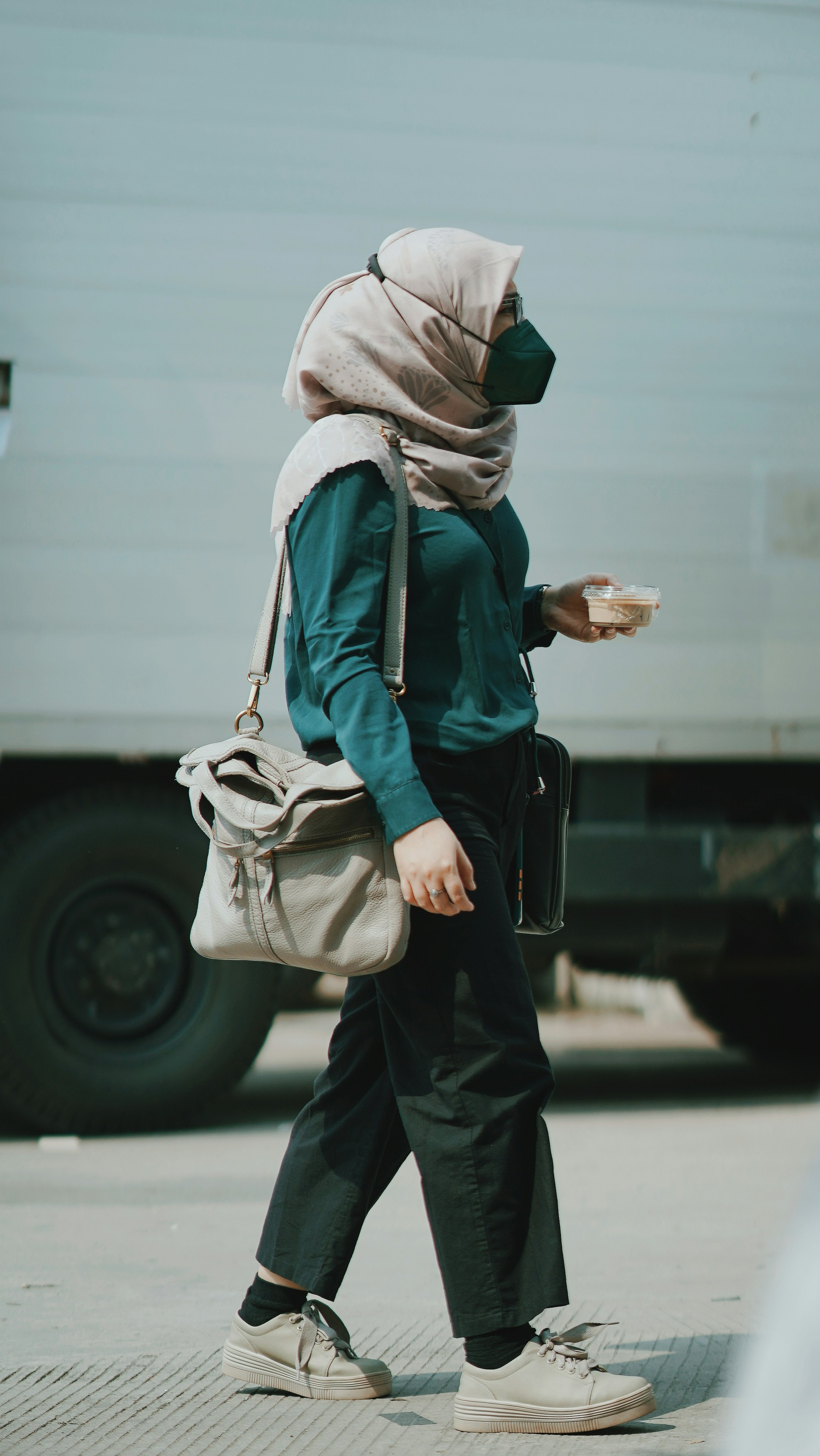 a woman walking down the street with a bag and a cup of coffee