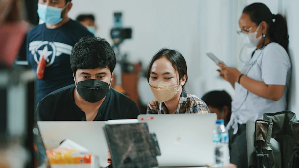 Modern office setting with professionals wearing PPE collaborating over digital devices.