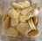 A clear plastic container filled with small, oval-shaped pieces of flatbread. The bread has a light brown, toasted appearance and appears soft and fluffy, with small air pockets visible on the surface. The container is positioned on a light, neutral background.