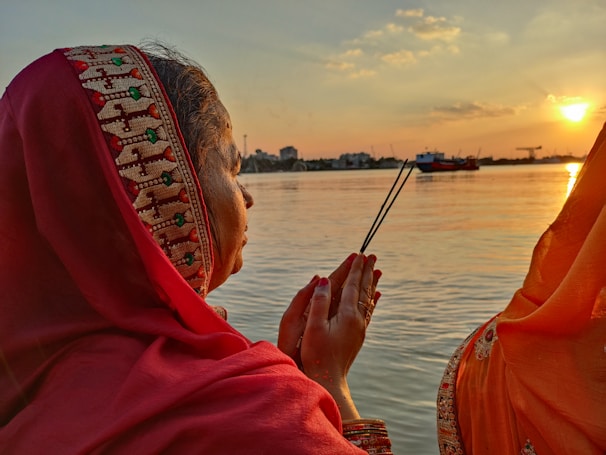 A peaceful scene of a person performing the tharpanam ritual by a riverbank at sunrise.