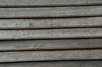 A series of horizontal wooden planks with visible grain patterns and small nail heads, displaying an aged and rustic texture.
