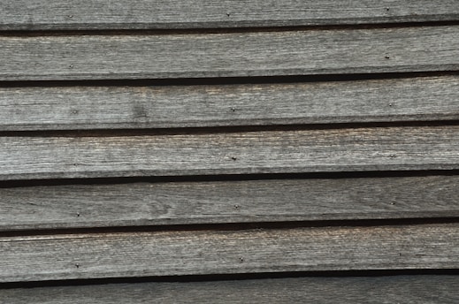 A series of horizontal wooden planks with visible grain patterns and small nail heads, displaying an aged and rustic texture.