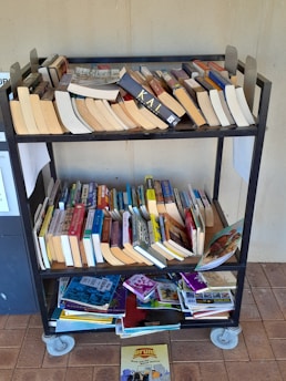 A sturdy metal book trolley filled with books, positioned next to a comfortable reading chair.
