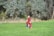 A woman and two children, all dressed in matching red and black plaid outfits, are standing together on lush green grass. They are surrounded by tall trees with dense foliage, creating a natural and serene setting.