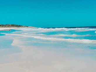 A serene white sandy beach on the Kenyan coast with turquoise waves gently lapping the shore.