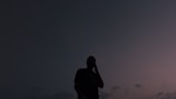 A silhouette of a lone figure against a dusky sky with deep blue tones.