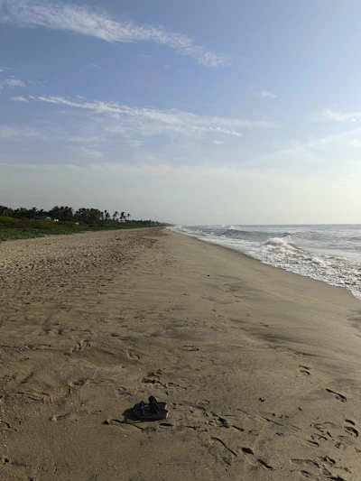 A sunlit beach scene with colorful sandals lined up on soft white sand near gentle ocean waves.