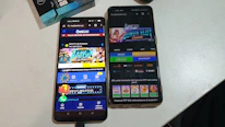 Two smartphones are displayed on a white surface, both showing gambling websites with colorful graphics, text, and various options for logging in and accessing games. The screens are bright and filled with promotional content related to casino and slot games.