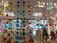 A colorful display of various hanging paper decorations, including hearts, circles, butterflies, stars, and owls. The decorations are suspended from the ceiling in multiple rows and layers, creating a vibrant and festive atmosphere. The background features a store setting with windows and shelves filled with various items.