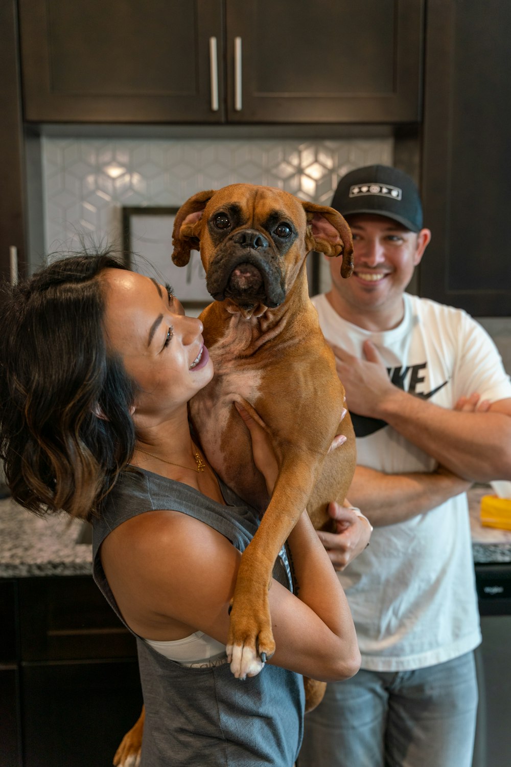 um homem e uma mulher segurando um cachorro em uma cozinha
