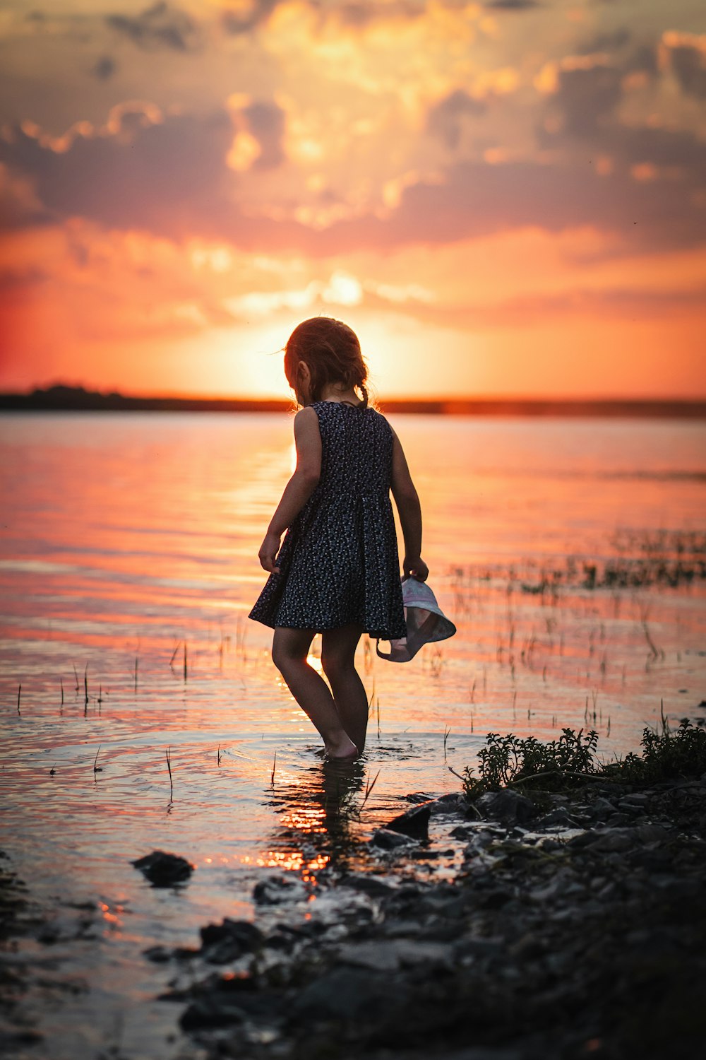 a little girl standing in the water at sunset