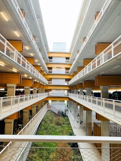 A multi-level parking structure with open walkways, wooden accents, and modern architecture. The center features a green area with plants and grass, adding a touch of nature.