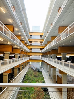 A multi-level parking structure with open walkways, wooden accents, and modern architecture. The center features a green area with plants and grass, adding a touch of nature.