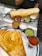 A South Indian meal featuring two large plates with dosas and accompanying chutneys. The dosas are crisp and golden brown, served with an assortment of small bowls containing colorful chutneys and sambar. The setting includes a restaurant table with glass cups and cutlery.