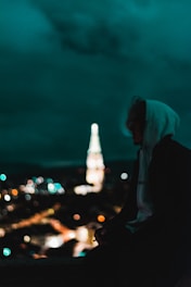 Black and white photo of a city skyline at night with a lone figure wearing a hoodie, embodying urban style.