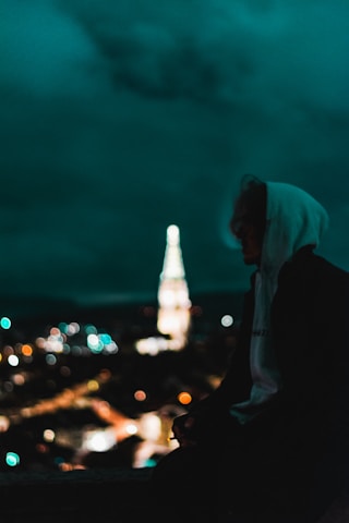 Black and white photo of a city skyline at night with a lone figure wearing a hoodie, embodying urban style.
