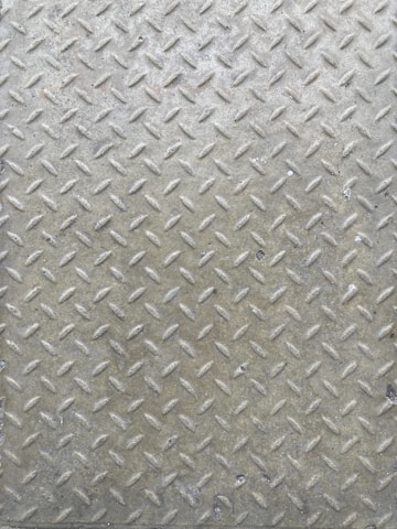 A textured metal surface featuring a diamond plate pattern with raised ridges, often used for slip resistance. The surface appears worn and has a slightly tarnished appearance from frequent use.