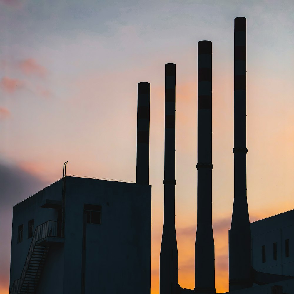 a building with three smoke stacks in front of a sunset