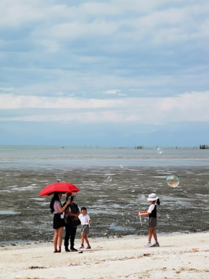 A family relaxing under a large red canopy at a sunny beach setting.