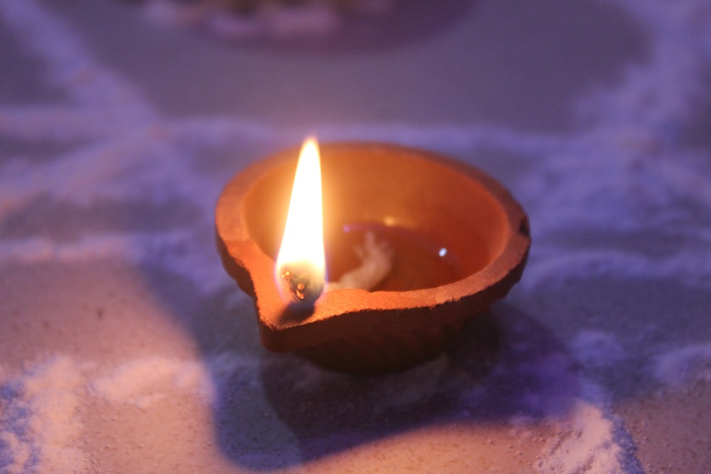 eine brennende Kerze, die in einer Schale auf einem Tisch steht