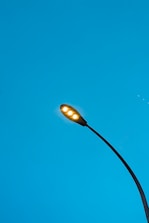 A streetlight with glowing lamps against a clear blue sky, featuring a sleek, modern design with a curved pole extending upwards.