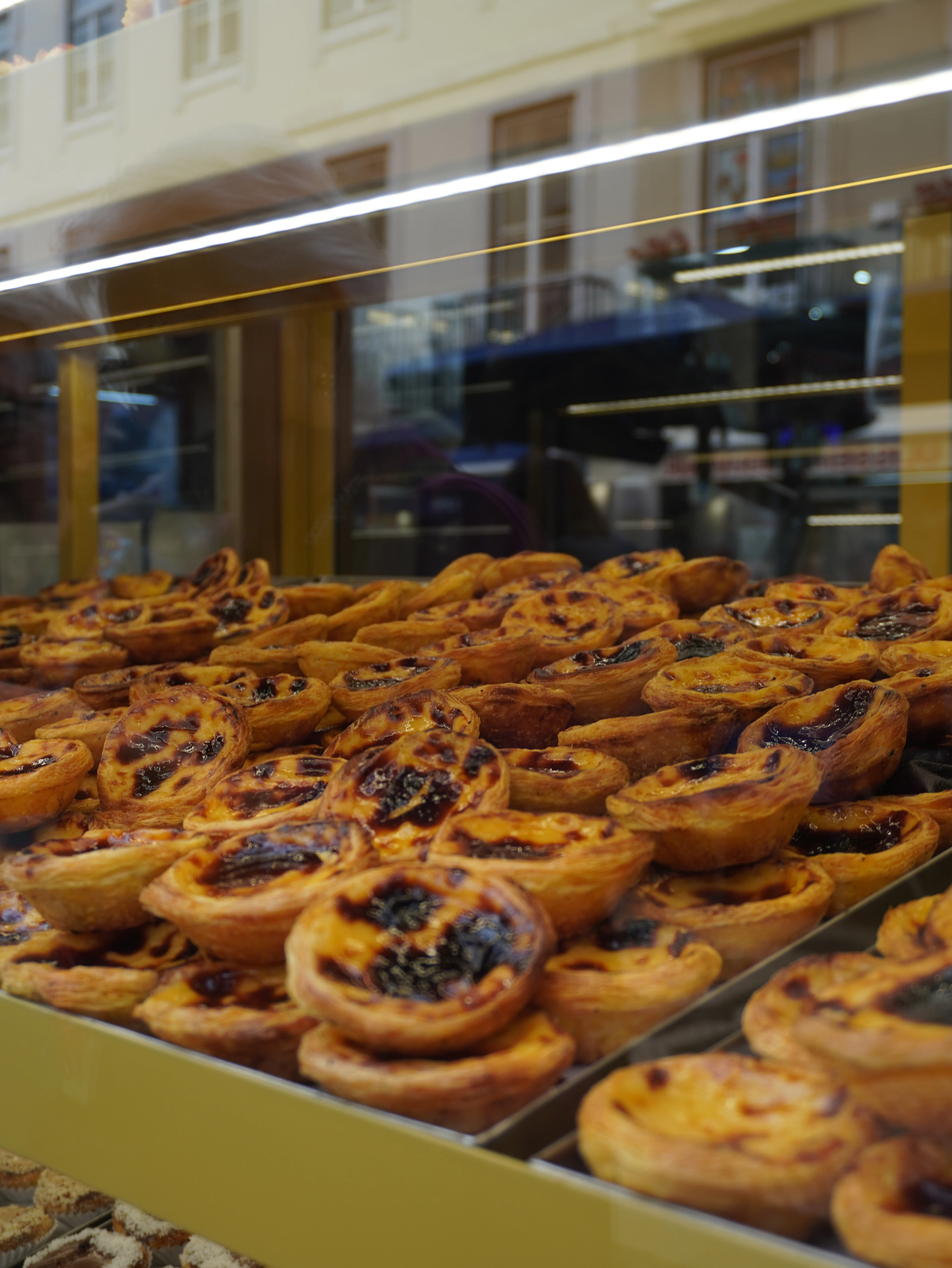 Trays of pasteis de nata, Portuguese custard tarts, stacked in a bakery window in Lisbon