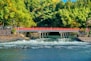 a red bridge over a river next to a forest