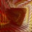 A digital abstract art piece characterized by swirling and layered textures. The predominant colors are warm reds, yellows, and oranges, creating a sense of depth and movement. The patterns are intricate, resembling folds or waves.