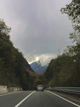 A luxury car driving along a winding mountain road with the sea visible in the background.