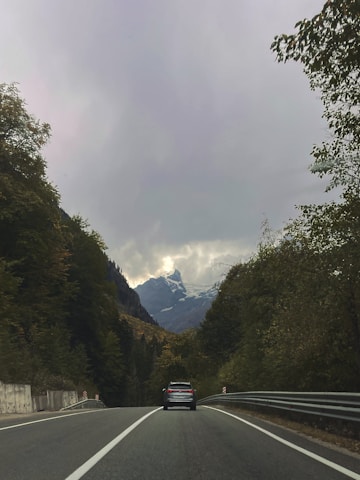 A cozy vehicle winding through Himachal Pradesh’s forested mountain roads under a clear blue sky.