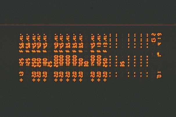 Rows of glowing orange alphanumeric characters in a pattern, resembling a digital or retro display, set against a dark background.