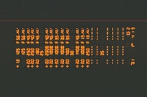 Rows of glowing orange alphanumeric characters in a pattern, resembling a digital or retro display, set against a dark background.