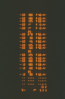 Rows of orange alphanumeric data appear against a dark background, resembling a digital or electronic display with numbers and letters in a structured format.