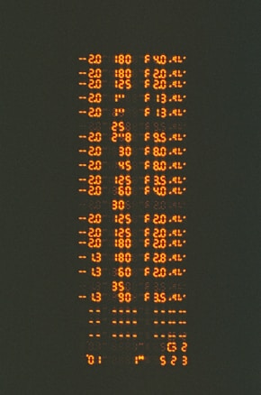 Rows of orange alphanumeric data appear against a dark background, resembling a digital or electronic display with numbers and letters in a structured format.