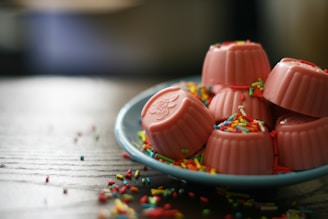 Pink molded candies are stacked on a blue plate, surrounded by colorful sprinkles scattered across the table.