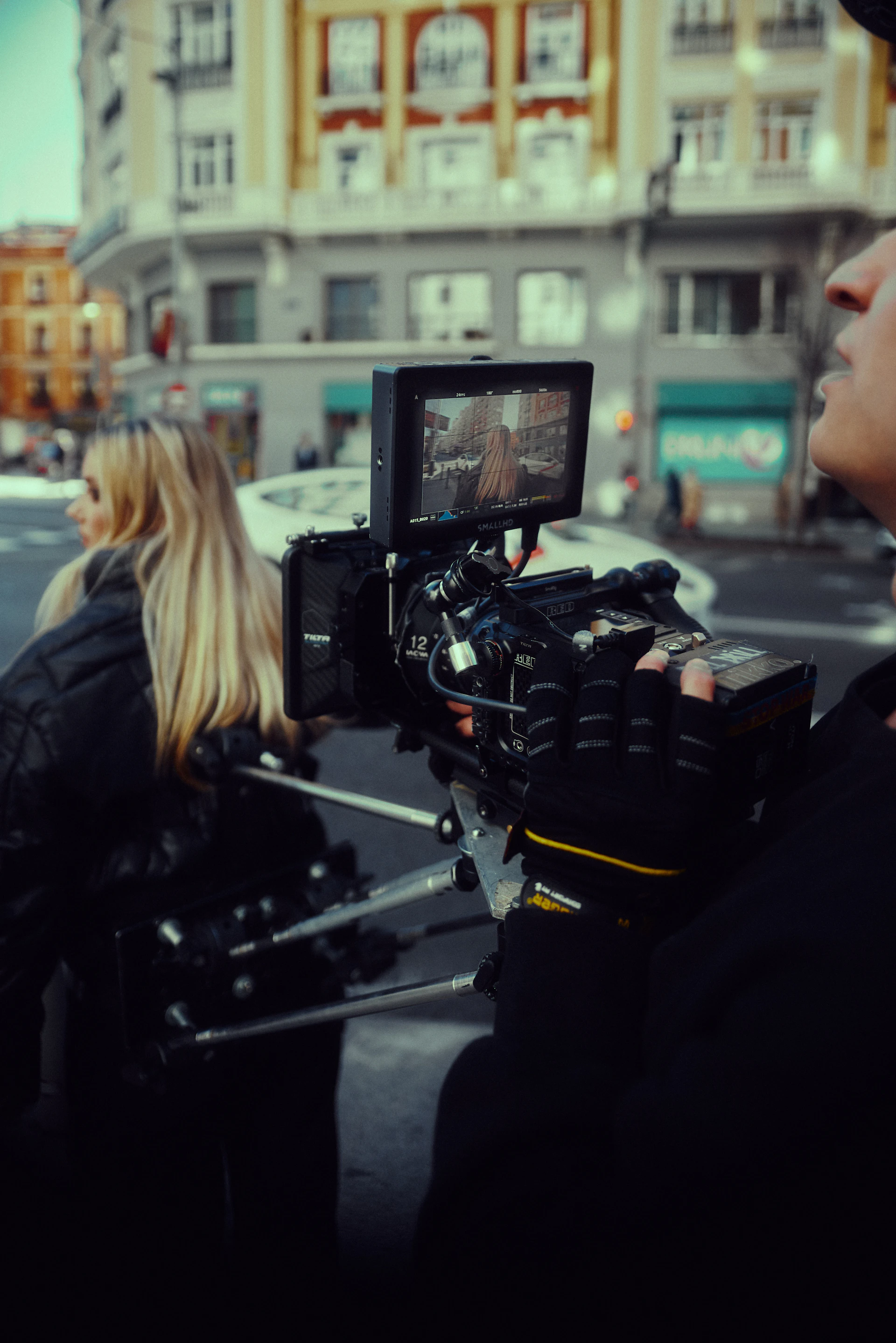 A close-up of a video camera recording a breaking news scene on a busy city street.