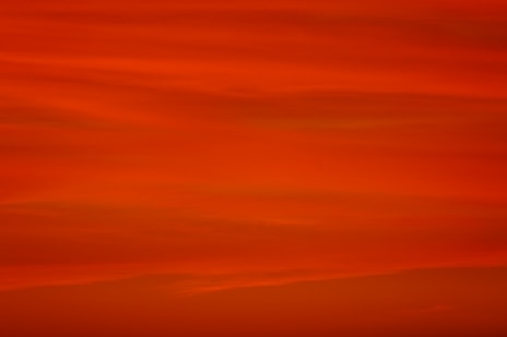 a red sky with a plane flying in the distance