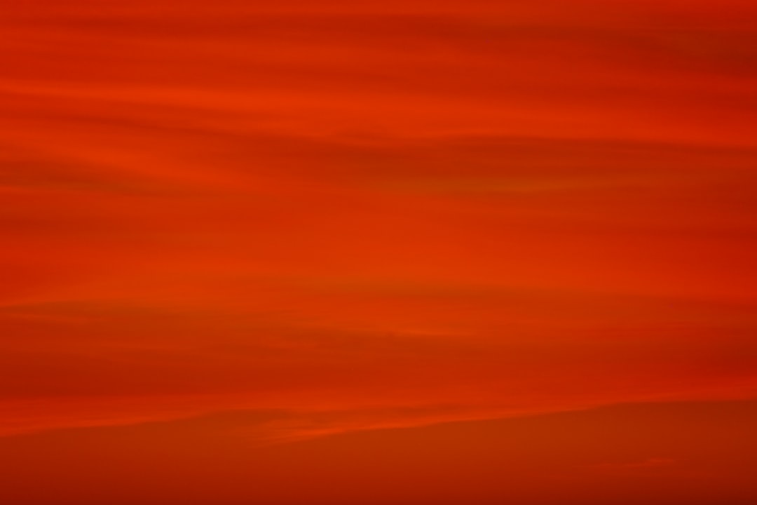 a red sky with a plane flying in the distance,