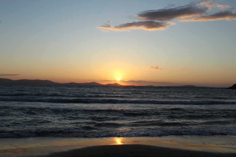the sun is setting over the ocean on a beach