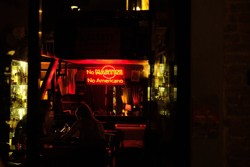 a person sitting at a table in front of a neon sign